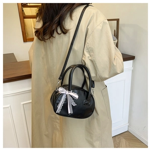 Detalle de bolso Boston negro con lazos rosas llevado por modelo con gabardina