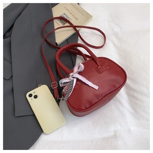 Detalle de bolso rojo con lazo de encaje rosa y relieve sobre sábana de lino blanca