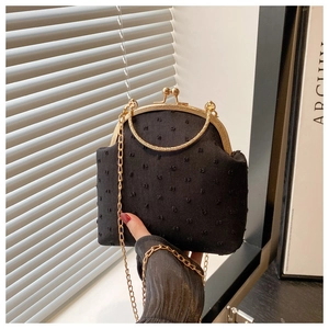 Détail d'un sac vintage noir texturé avec chaîne dorée et poignée en anneau métallique