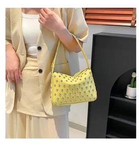 Sac à bandoulière en cuir jaune vif avec clous rivetés argentés porté par une personne