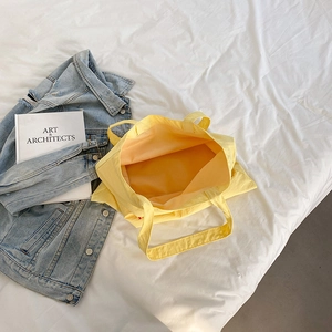 Detail of spacious bright yellow nylon tote bag with red tag on a white bed sheet