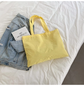 Flat lay of a yellow nylon tote bag with denim jacket and book on white sheets
