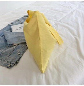 Detail view of a yellow nylon tote bag on a bed with denim jacket and books