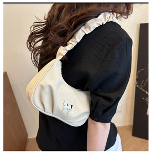 Close-up of beige pleated crescent bag with silver butterfly charm decoration