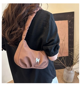 Detail of coffee canvas pleated crescent bag featuring silver butterfly metal ornament