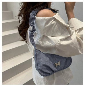 Détail latéral d'un sac hobo en jean bleu avec papillon argenté et bandoulière plissée