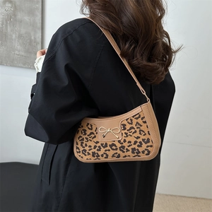 Leopard print underarm bag with gold bow and khaki leather strap on model shoulder
