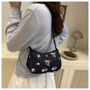 Dettaglio della borsa baguette nera con fiocchi rosa e stampe di rose indossata dal modello