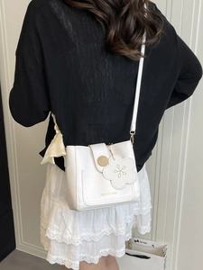 Sac bandoulière blanc minimaliste avec boucle en bois et pendentif fleuri sur un modèle