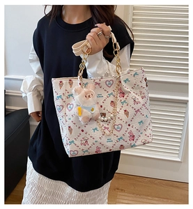 Detail of white tote bag with cute cartoon prints, gold chain strap, and pearl charms