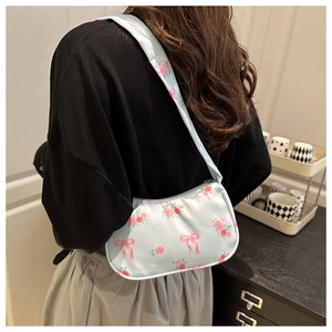 Dettaglio della borsa a spalla in raso azzurro con stampe di rose rosa e fiocchi su modella
