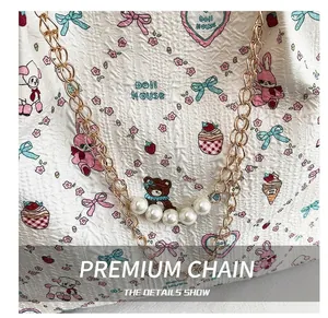Macro detail of golden metal chain strap with five white pearls on a cartoon pattern bag
