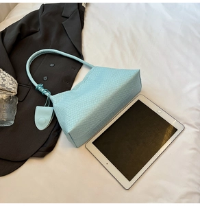 Détail du sac cabas tressé bleu clair avec motif en damier et breloque sur la poignée