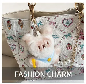 Close-up of cute pink plush bear charm with blue scarf and pearl chain on a tote bag