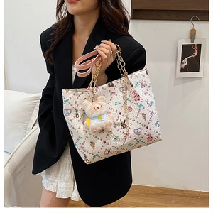 Detail of cartoon printed tote bag featuring plush bear charm and pink leather strap