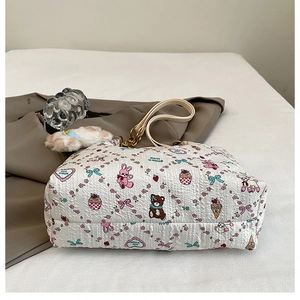 Detail of white quilted tote bag featuring cute cartoon patterns and plush charm