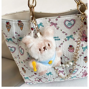 Close-up of white tote bag with textured fabric, cartoon prints and plush bear charm