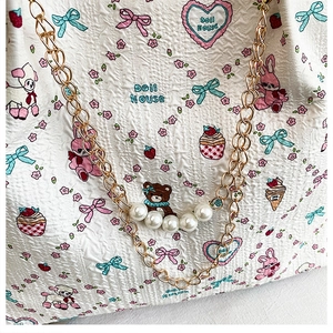 Close-up of white embossed tote bag with cartoon patterns and pearl gold chain straps