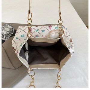 Detail of the white tote bag showing cartoon prints, chain strap, and inner zip pocket