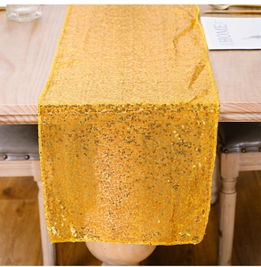 Dettaglio ravvicinato del runner da tavola con paillettes dorate su un tavolo di legno