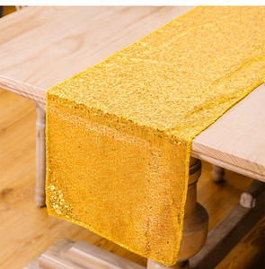Dettaglio del runner da tavola con paillettes dorate lucide su tavolo in legno rustico