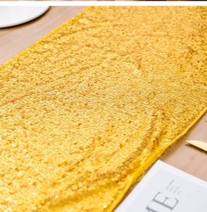 Dettaglio del runner da tavola con paillettes dorate su un tavolo di legno con posate