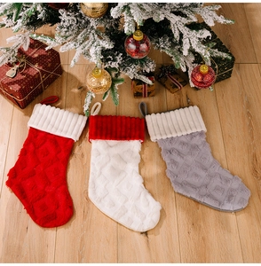 Tres calcetines navideños de felpa en rojo, blanco y gris sobre suelo de madera clara