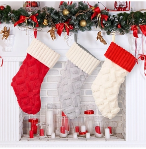 Vista de tres calcetines navideños de felpa en rojo, gris y beige en una chimenea blanca