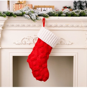 Primer plano de un calcetín navideño de felpa roja con rombos colgado en una chimenea blanca