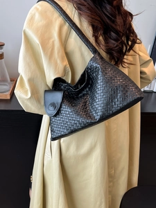 Sac à bandoulière chic en cuir tressé noir porté avec un trench-coat d'automne élégant
