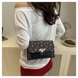 Detail of cherry pattern crossbody bag with gold lock and chain strap on shoulder