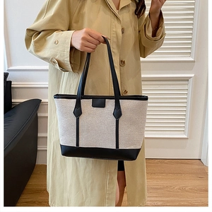 Detail of canvas tote bag with black leather handles shown in a modern interior setting