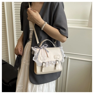 Detail of cream crossbody bag featuring lace trim, plaid bow, and dual buckle straps