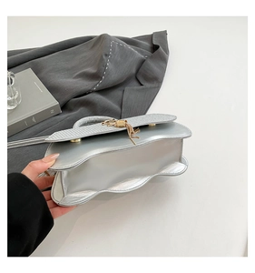 Detail of silver wavy handbag featuring golden tassel charm and magnetic snap flap
