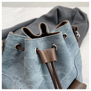 Close-up of blue denim bucket bag with brown leather drawstring and metal eyelet details
