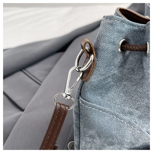 Detailed close-up of blue denim bucket bag with silver hardware and leather strap hooks