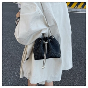 Detail of a black woven bucket bag featuring elegant pearl charms and silver metal chain