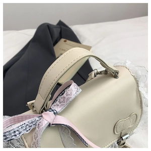Dettaglio della borsa in pelle PU crema con bordi in pizzo e fiocco di nastro rosa