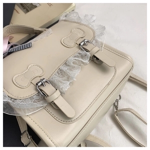 Dettaglio borsa beige in ecopelle con bordo in pizzo e doppie fibbie metalliche