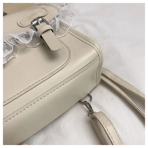 Détail macro du sac beige avec bordure en dentelle blanche et boucle en métal argenté