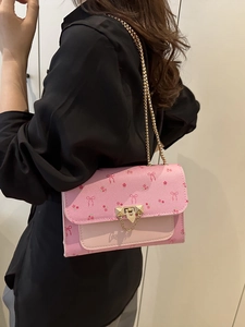 Sac bandoulière rose imprimé cerise avec chaîne dorée porté par un mannequin