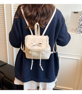 Detail of cream mini backpack featuring lace trim, leather bow, and drawstring tassels