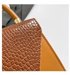 Detail of crocodile embossed leather handbag with golden metal hardware and sturdy handle