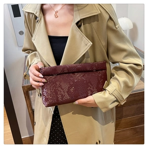 Detail of burgundy snakeskin texture on an elegant clutch bag held by a model