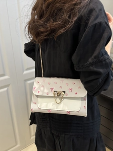 Sac bandoulière blanc motif cerise avec chaîne dorée porté par une femme en intérieur