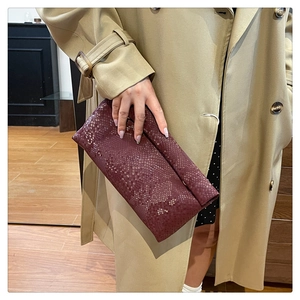 Close-up of elegant burgundy snakeskin clutch bag held with a classic beige trench coat