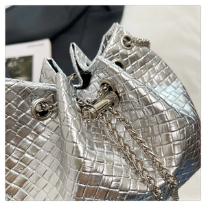 Detail showing metallic silver woven texture and drawstring chain closure on bucket bag