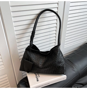 Detail of a black woven leather hobo bag with a knotted strap on a black sofa