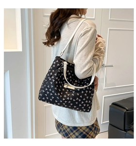 Side view of large black tote bag with bow prints worn by a model in a modern room