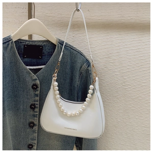 Detail of white PU crescent bag featuring faux pearl handle and gold metal hardware